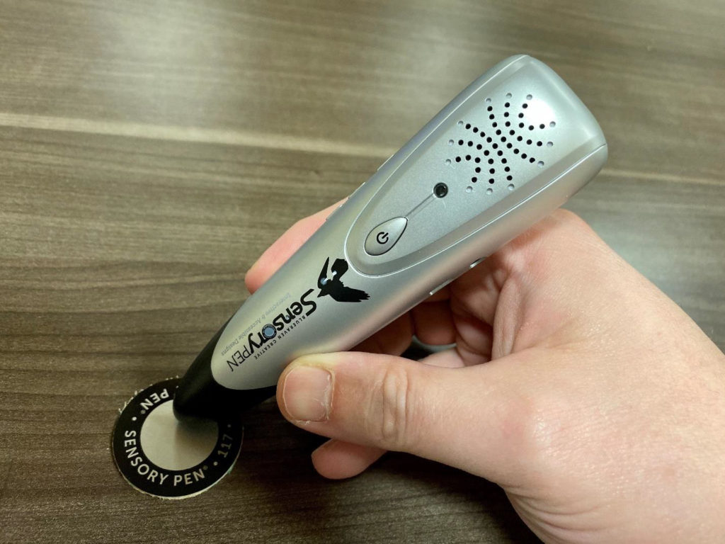 A handheld audio player shaped like a pen scanning a circular trigger