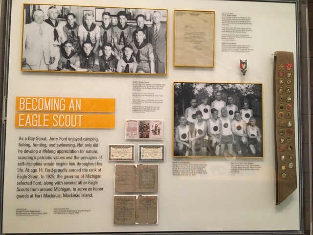 Photo shows the label discussed in this section. It says "Becoming an Eagle Scout" in white letters on orange backgrounds. Photos and artifacts are floating in the case next to the text with orange color borders or frames around them.